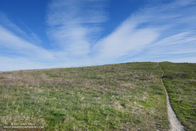 blue sky, sunshine, high clouds and a trail on a hill