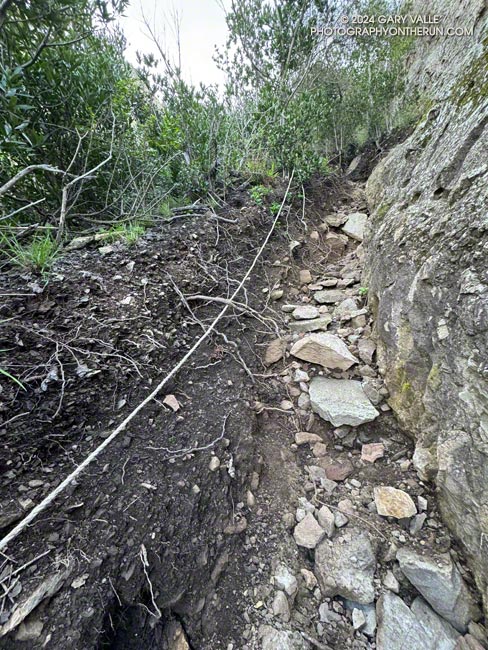 A steep, rocky gully on the Western Ridge route. The rope is an unnecessary and recent addition. The gully ends at a low-angle face with big hand and foot holds. April 7, 2024.