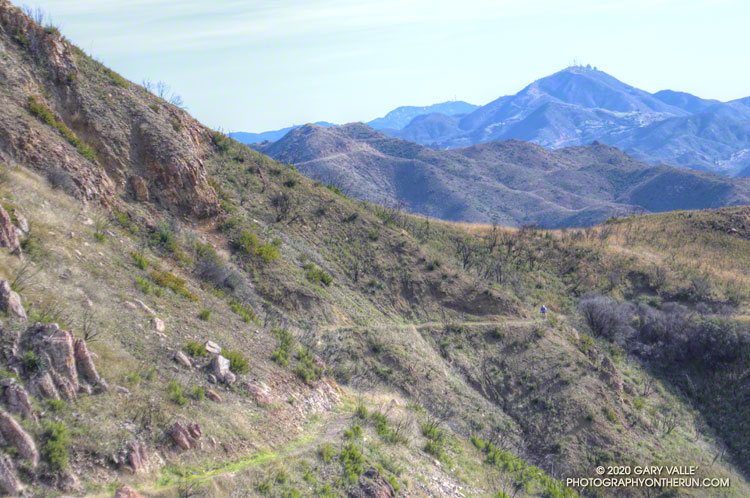 A westbound mountain biker works up the Backbone Trail on the last significant climb before the descent to Yerba Buena Road and the Mishe Mokwa Trailhead. Castro Peak and Saddle Peak can be seen in the distance. The Backbone Trail passes near both of these peaks.