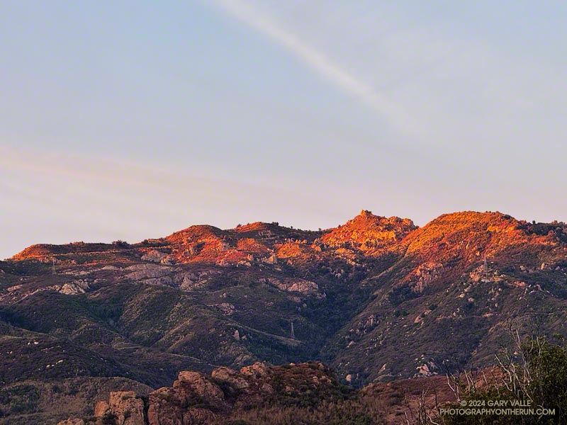 The red-tinged light of the rising sun on Castro Crest in the Santa Monica Mountains. The top of Bulldog Mtwy Fire Road is near the skyline in the cetner of the image.